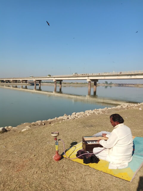 A man on a river bank with his music instruments for money